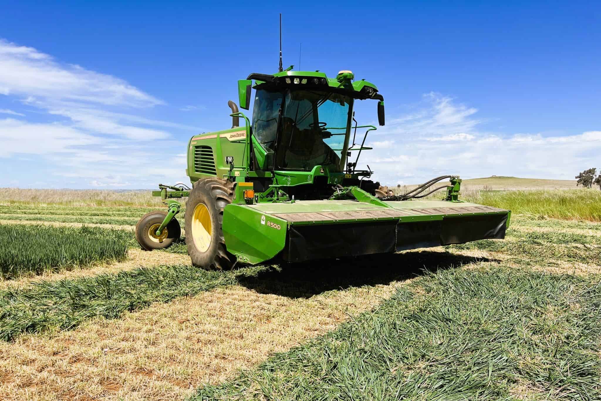 Large green farm equipment sits in a green paddock with freshly cut hay